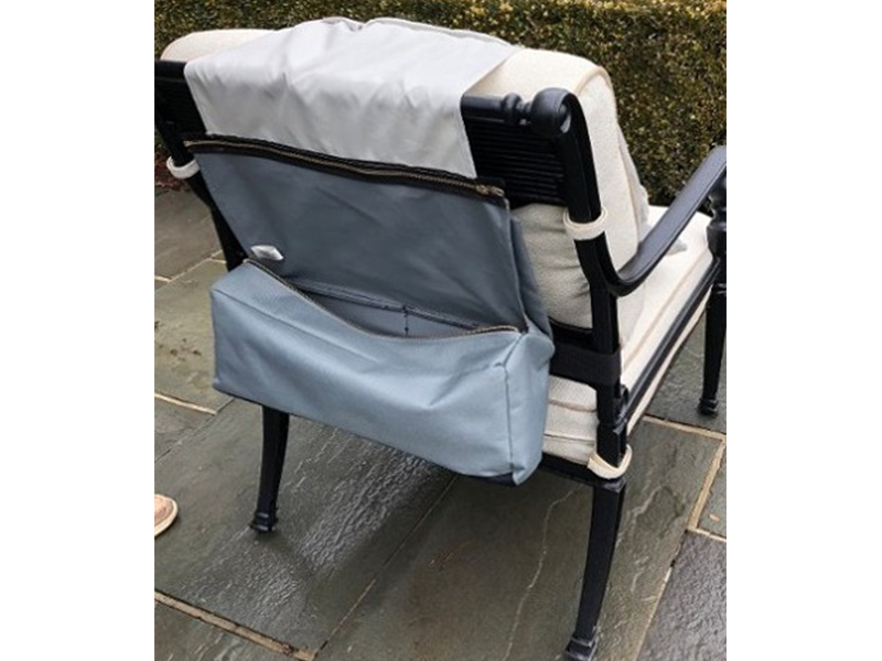 A gray zippered bag attached to the back of a black and white outdoor chair. The chair is set on a stone patio.