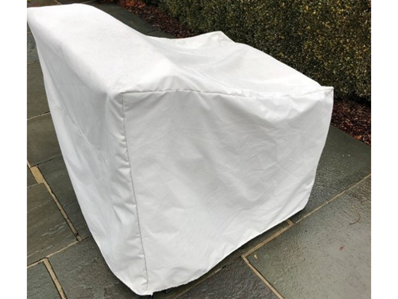 White chair cover on a chair, outdoors on stone tiles, with bushes in the background.