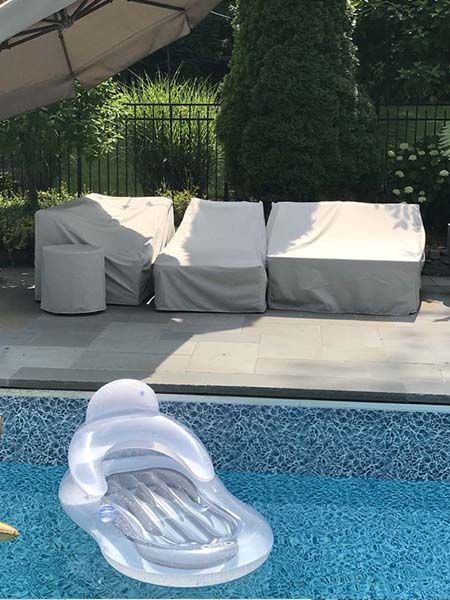 Pool with a floating inflatable lounge chair. Covered patio furniture sits in the background.