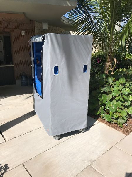 Covered cart on wheels, outside on a paved surface. Gray cart cover with blue handles.