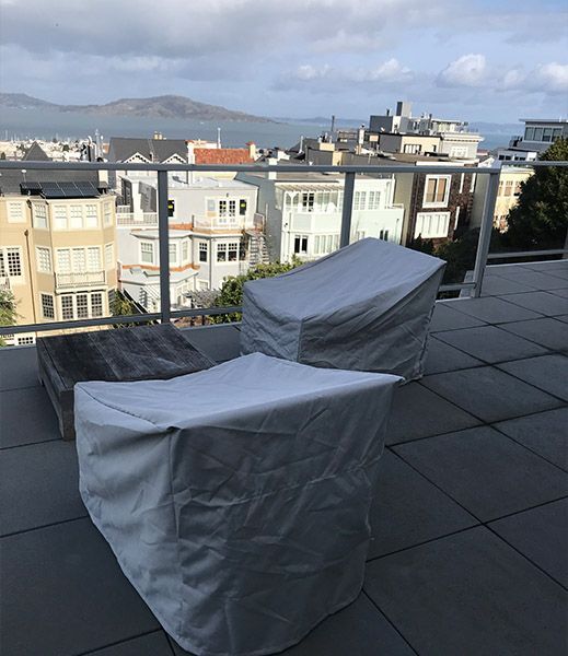 Rooftop patio with covered furniture, overlooking a city with a view of hills and cloudy sky.