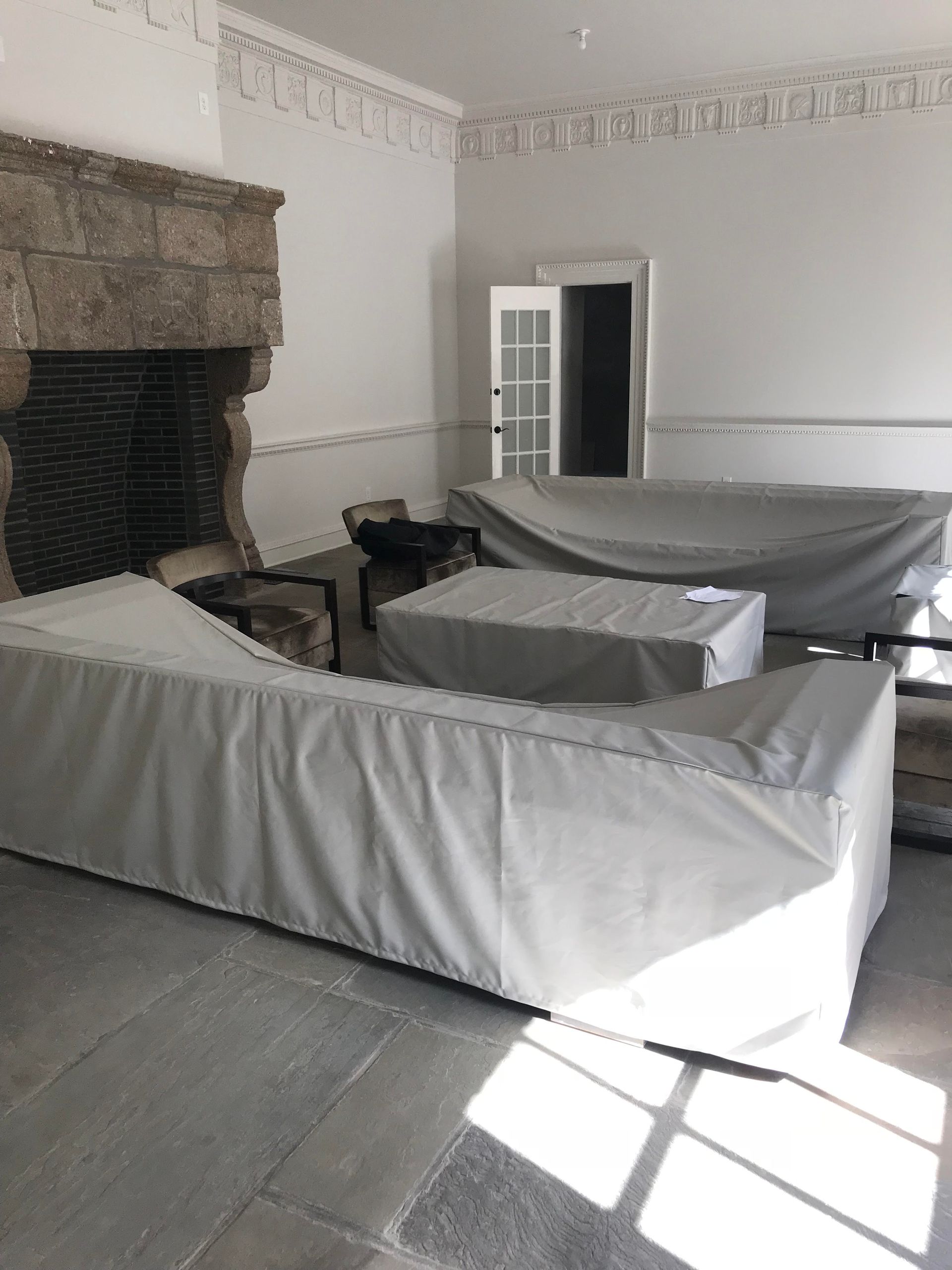 An empty room with stone fireplace and covered furniture, likely awaiting renovations or new setup.