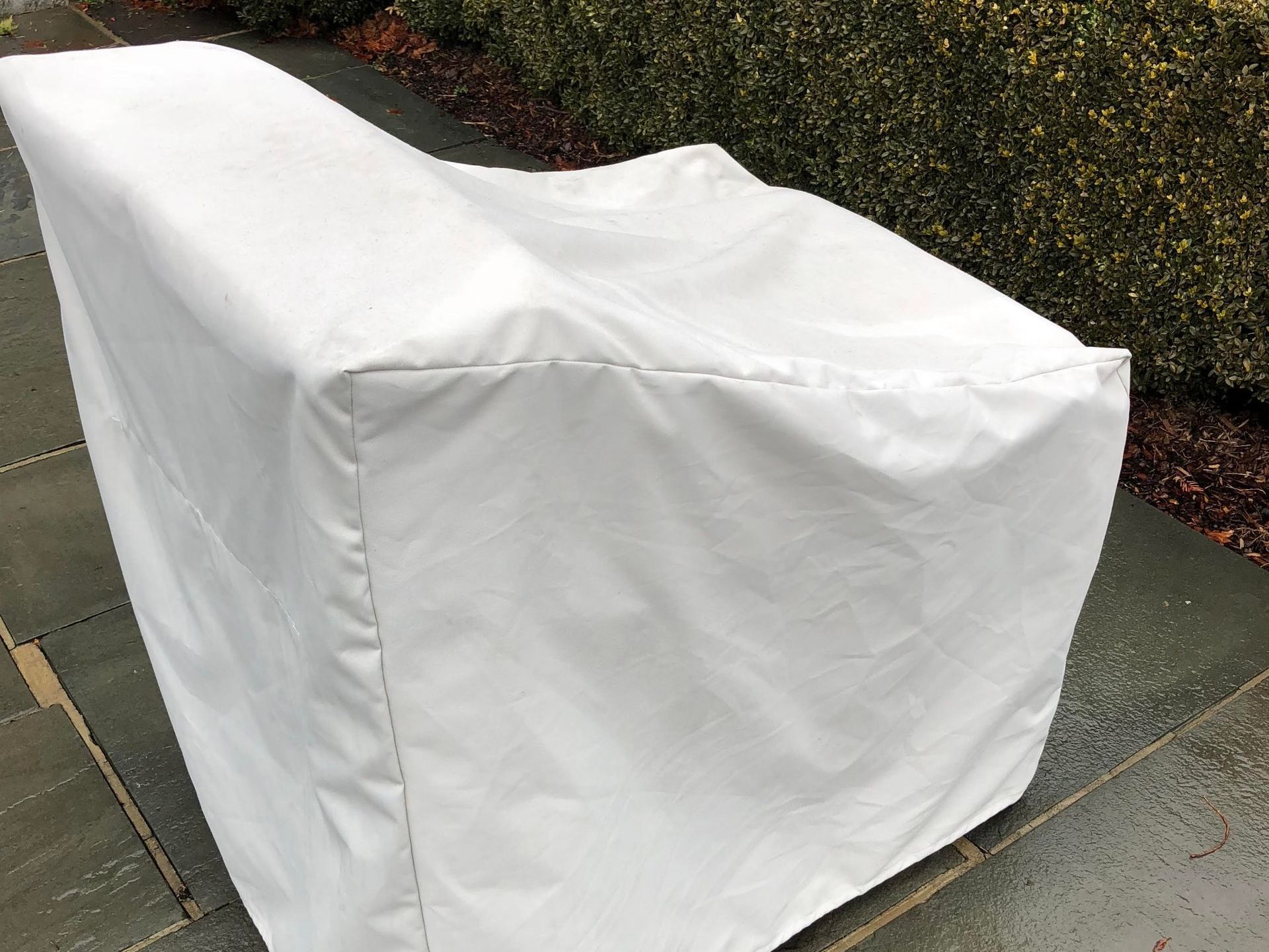 White outdoor furniture cover on a stone patio. The cover is draped over a chair, obscuring its shape. 
