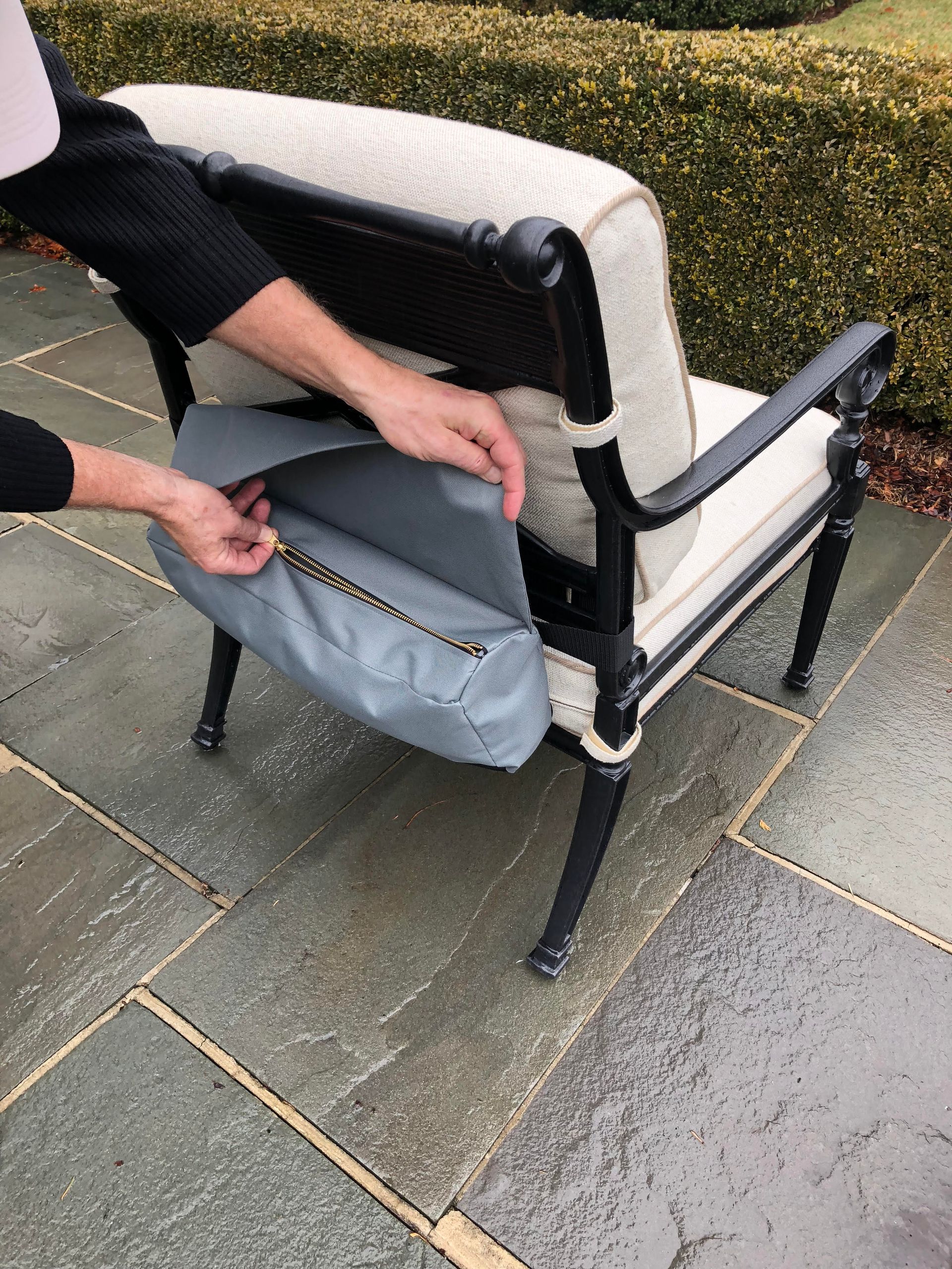 Person placing a grey bag with a zipper into a black and white chair on a stone patio.