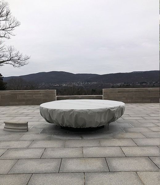 A large, covered circular stone structure sits on a paved patio overlooking a distant mountain range under a gray sky.