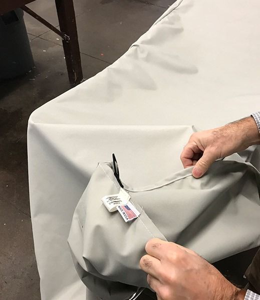 Hands holding up a light beige table cover with a tag that says 
