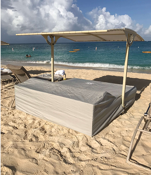 A covered, rectangular beach bed with a canopy on a sandy beach next to the ocean. The sky is cloudy.