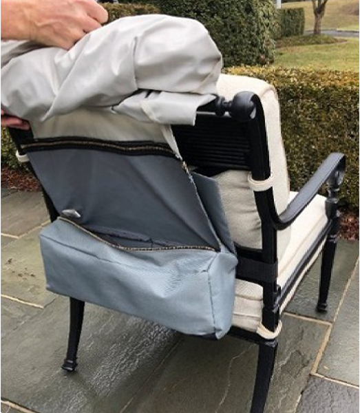 Person placing a light gray bag over the back of a black and white outdoor chair. Bag has a zippered compartment.