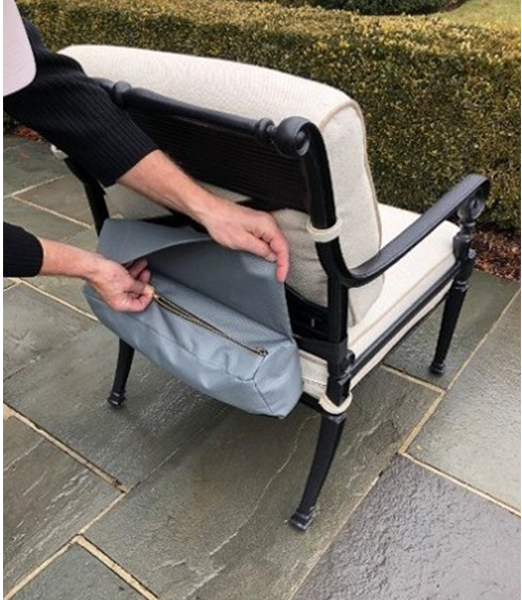 A person inserts cushions into a gray zippered bag behind a black and white outdoor chair on a stone patio.