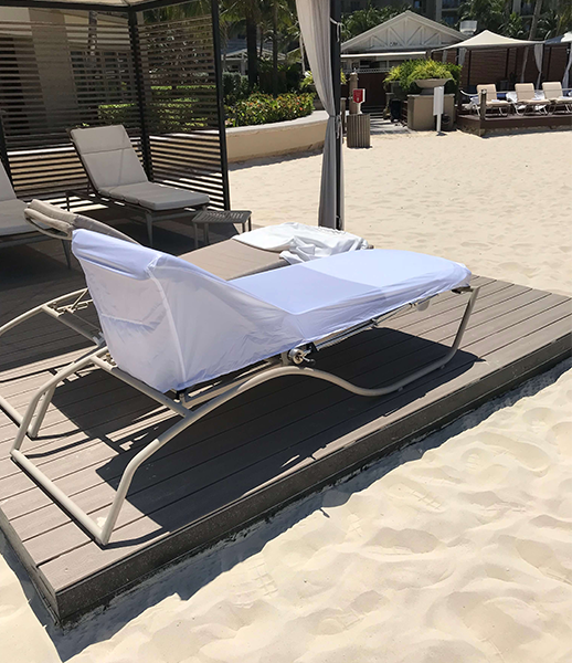 Beach chair with white cover on a wooden platform, on a sandy beach.