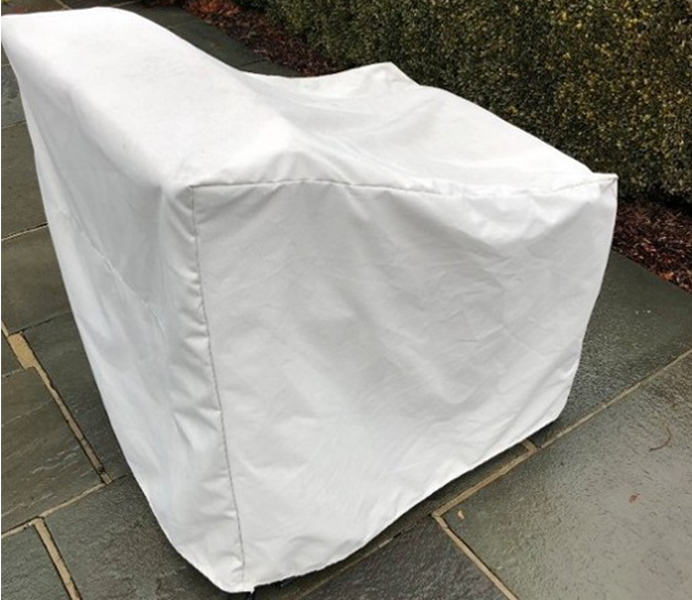 White chair covered with a white protective cover sits on a paved stone surface next to a hedge.