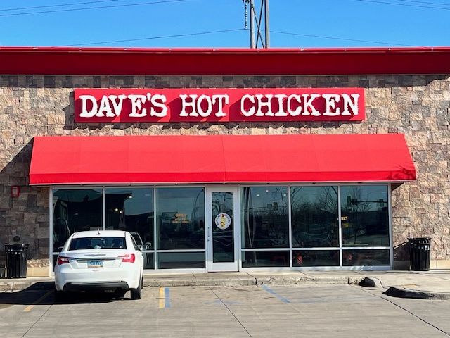 A white car is parked in front of a dave 's hot chicken restaurant.