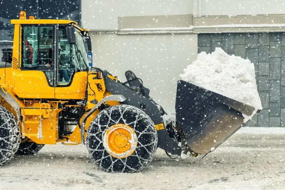 Heavy yellow industrial loader clearing a large pile of snow.