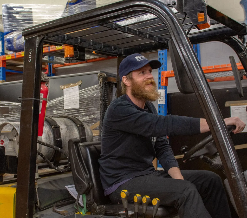 A man with a beard is driving a forklift in a warehouse