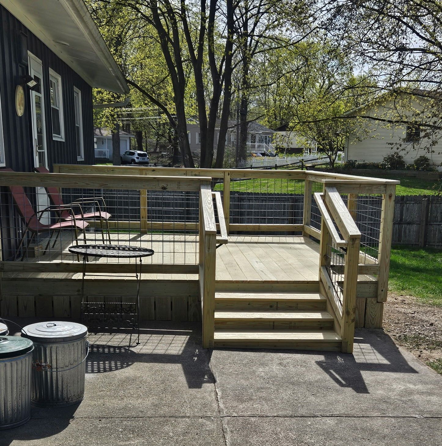 Wooden deck with stairs and railing outside a house; trash cans in the foreground.