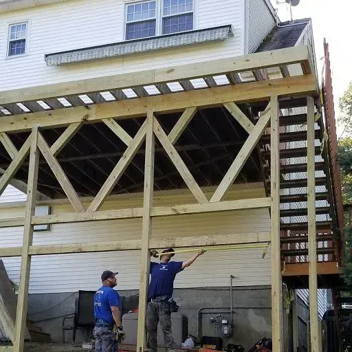 Two men measure a wooden deck frame under construction against a white house.