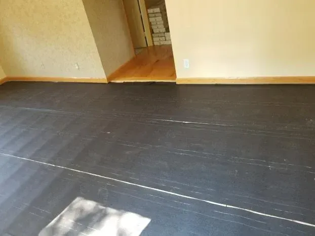 Black flooring in a room with beige walls and a doorway with hardwood floors.