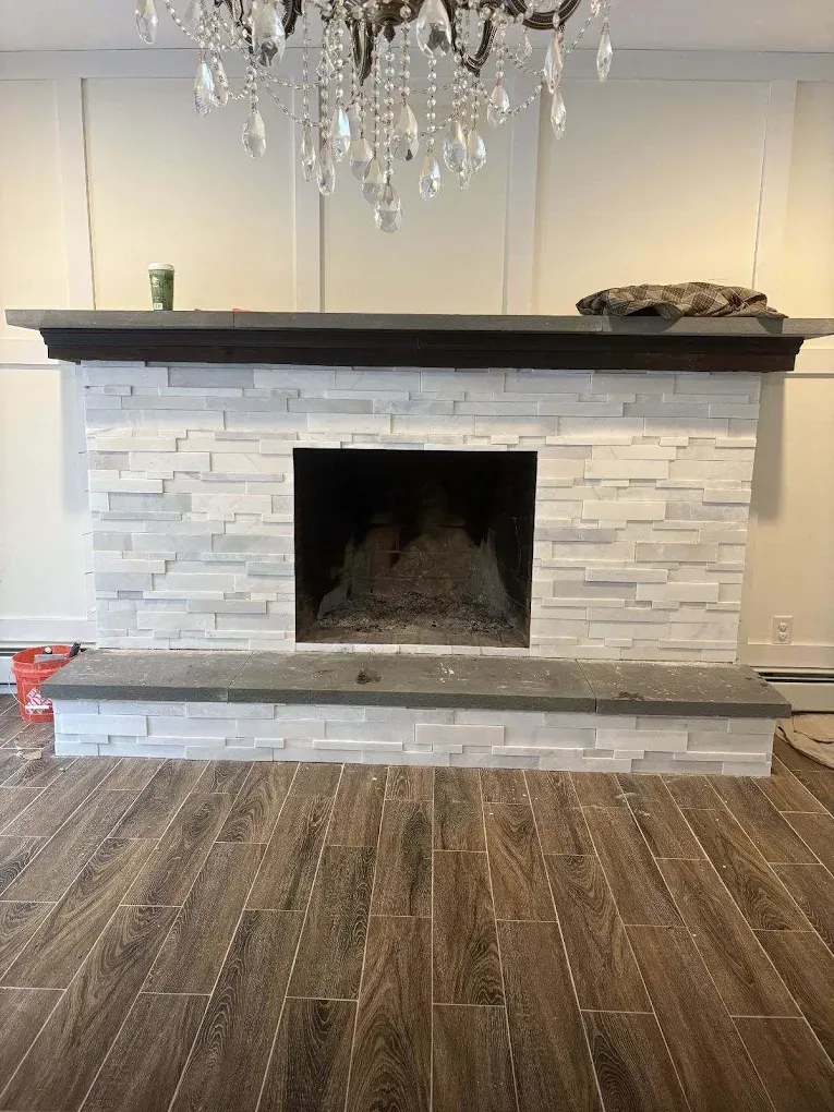 Fireplace with white stacked stone, dark gray mantle, and wood-look tile floor.