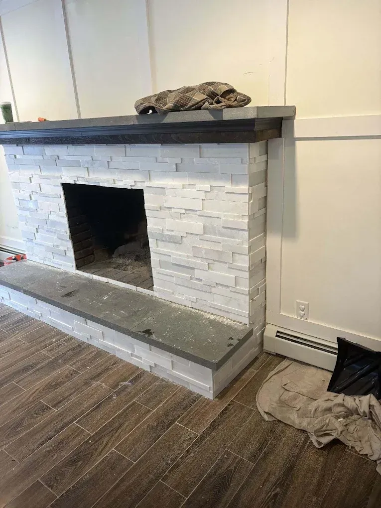 Fireplace with light gray stacked stone, dark gray top and hearth, and wooden mantle.