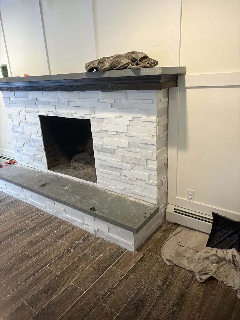 Fireplace with white stone facade, dark mantle, and grey hearth, in a room with wood floors.