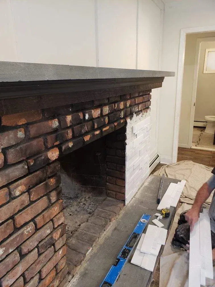 Brick fireplace with gray mantel being renovated; person in frame.