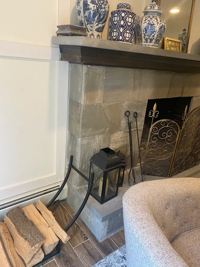 Fireplace with stone facade, firewood, and blue and white vases on the mantel.