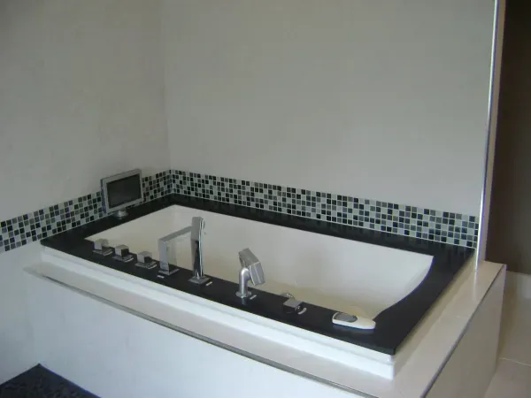 A modern, white bathtub with black trim and tile surround in a white bathroom.
