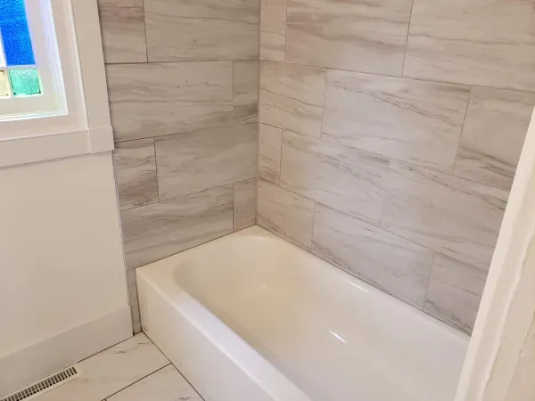 Bathroom with a white bathtub, tiled walls, and a stained glass window.