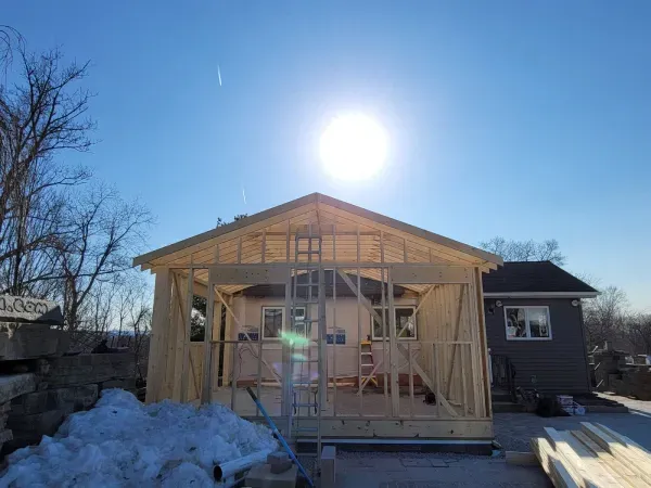 Construction of a wooden building on a sunny day. Frames and roof are visible with blue sky and sun overhead.