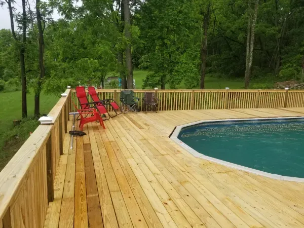 Wooden deck with a pool and trees, red chairs on the deck.