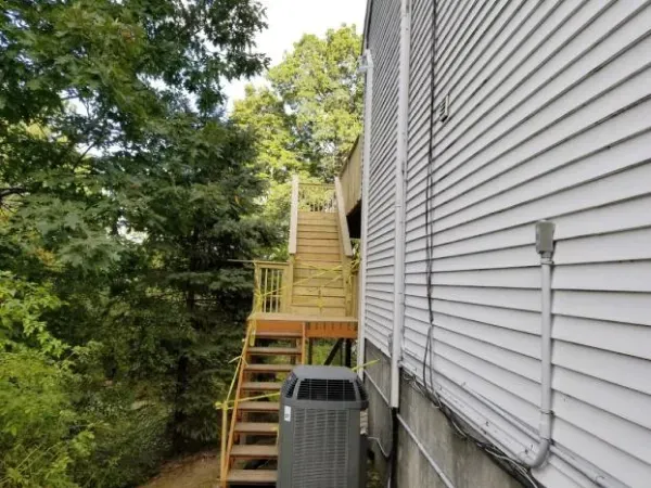 Wooden stairs leading up to a deck next to a white-sided building. An AC unit sits below.