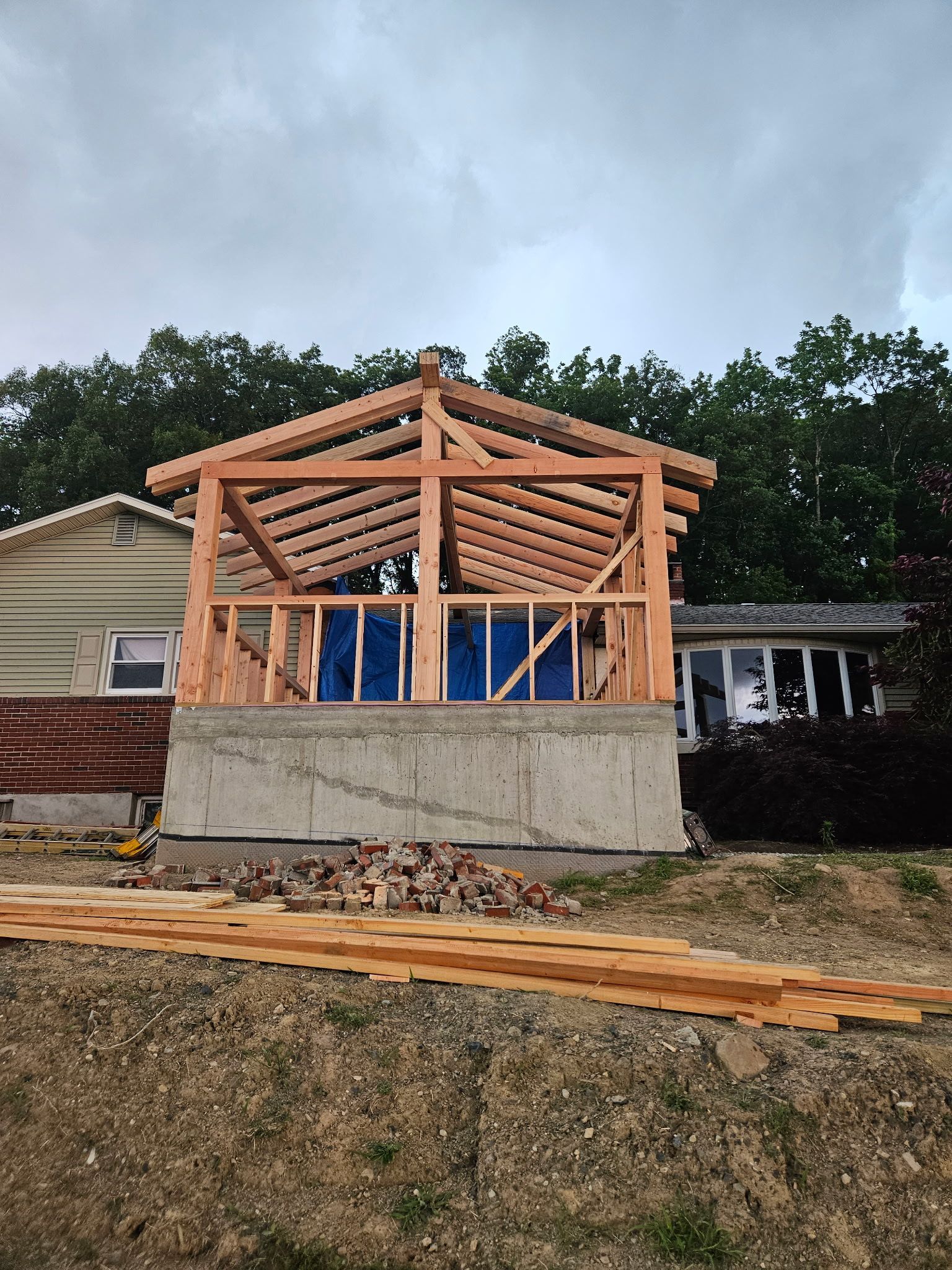 Wooden structure under construction atop a concrete base, against a house.