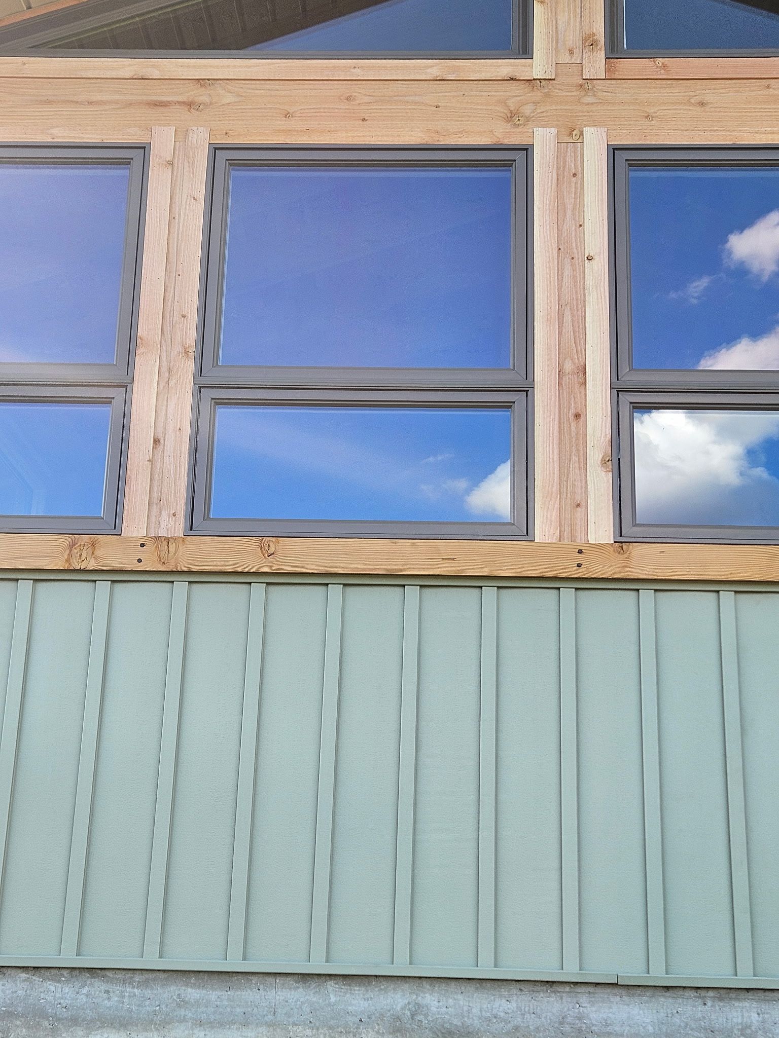 Blue sky reflected in rectangular windows above green vertical siding.