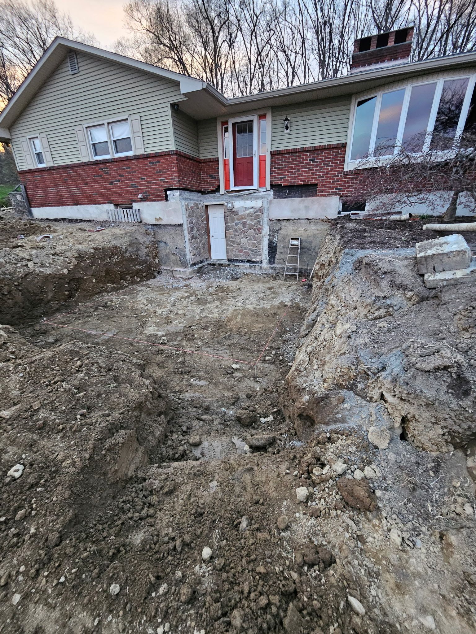 A house undergoing construction; a deep trench dug in front of a brick and siding facade.