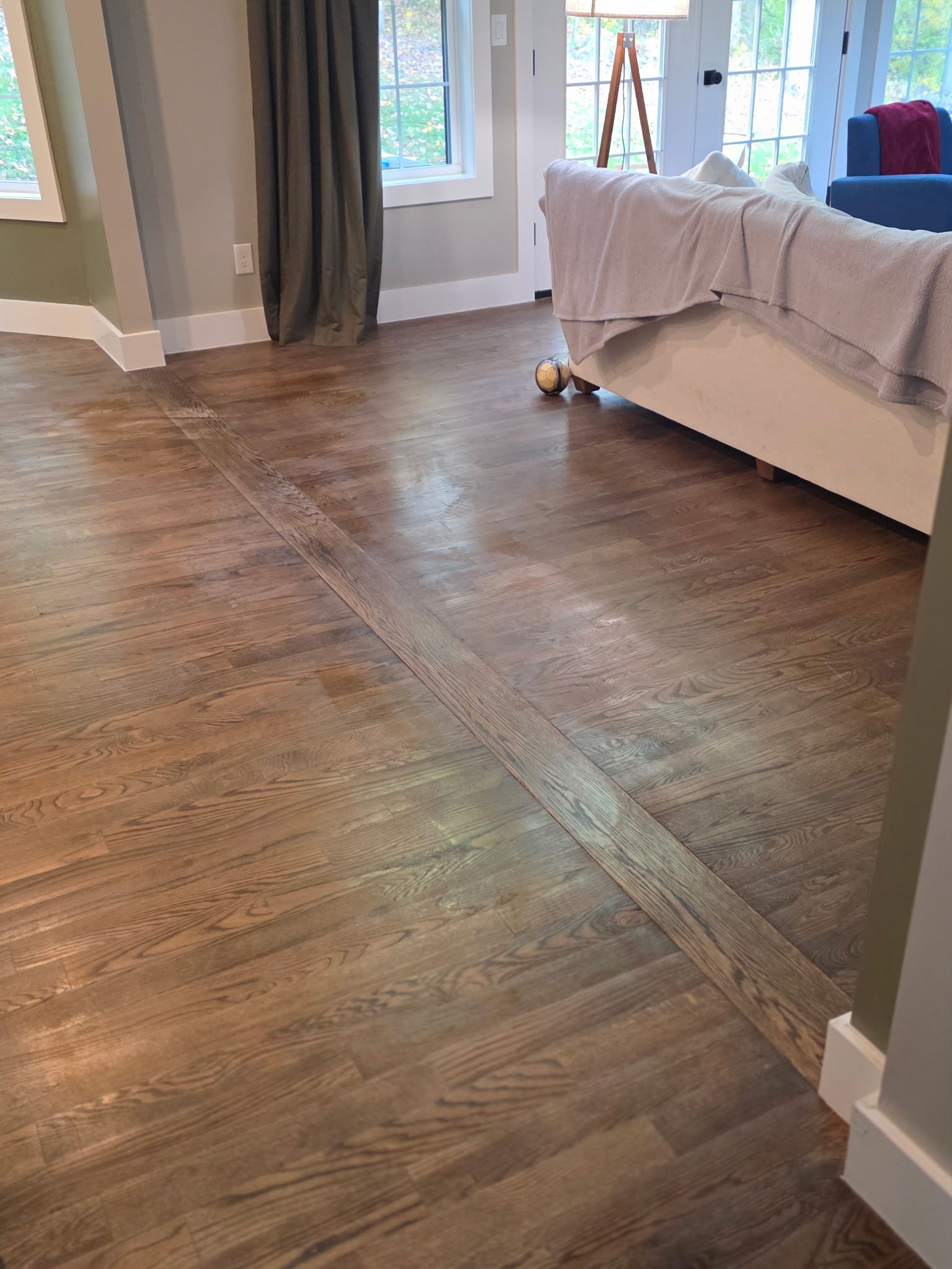 Wood flooring in a room with a white couch, green wall, and grey curtains.