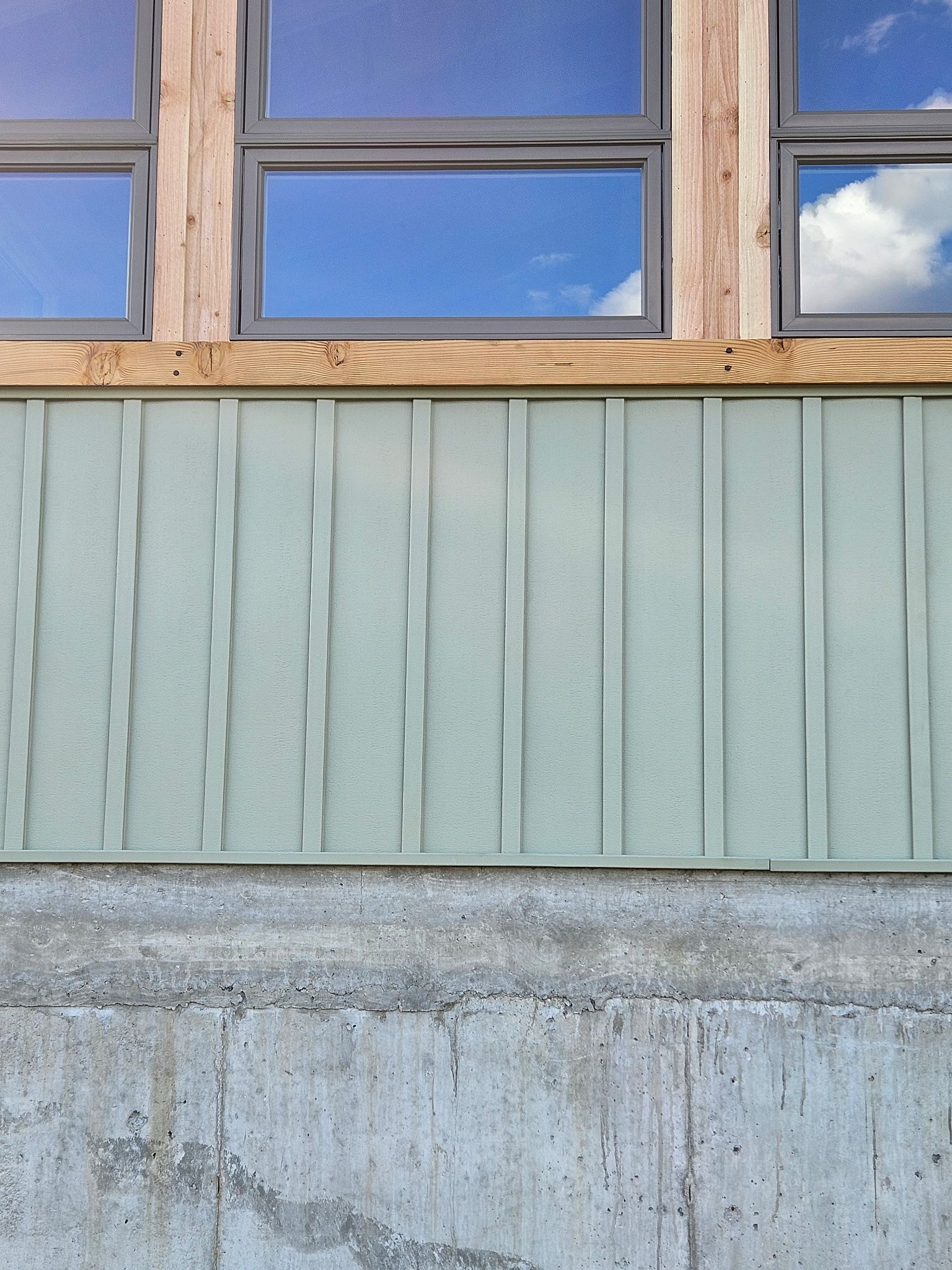 Exterior view of a building with windows reflecting a blue sky. Green siding over concrete foundation.