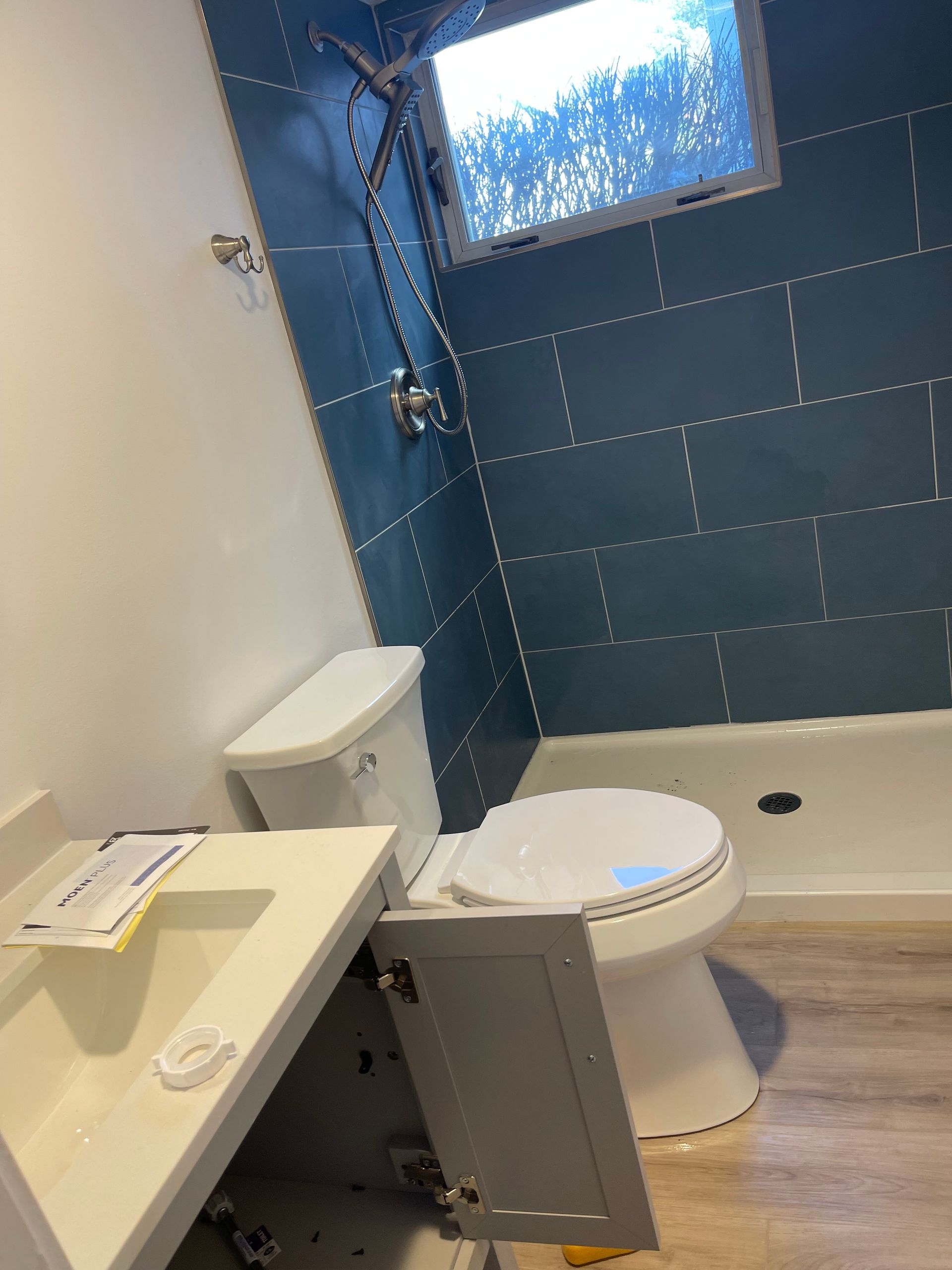 Bathroom with blue tiled shower wall, toilet, vanity, and window.