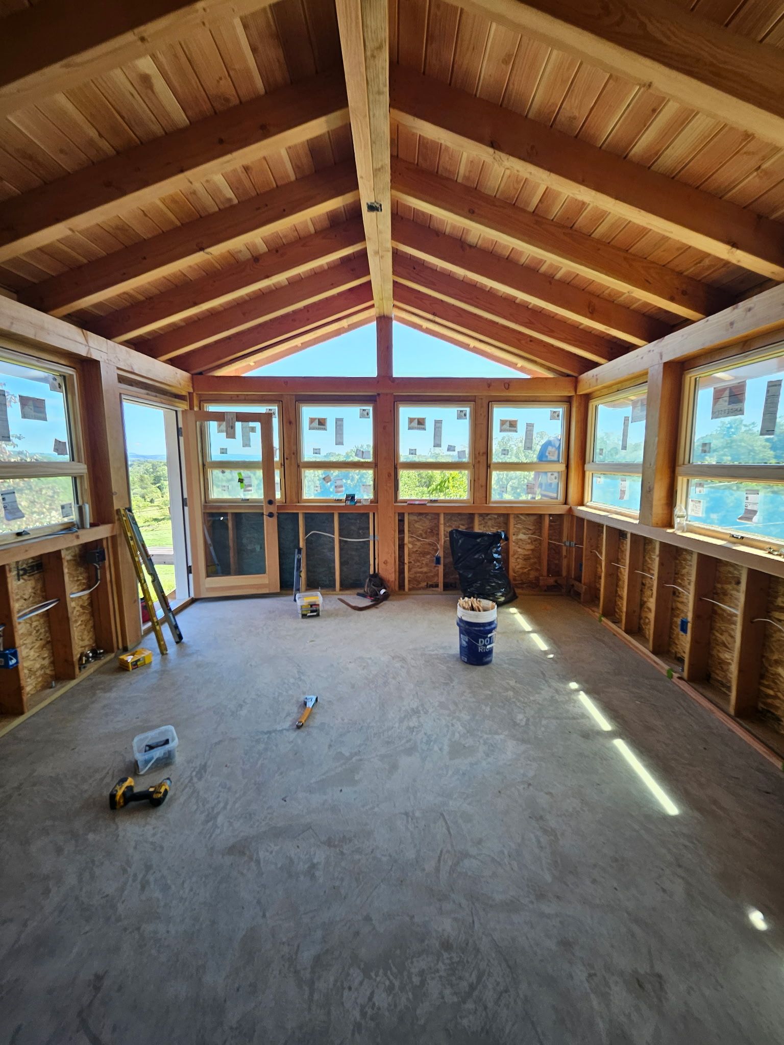 Interior of a sunroom under construction, showcasing wooden beams and window frames.