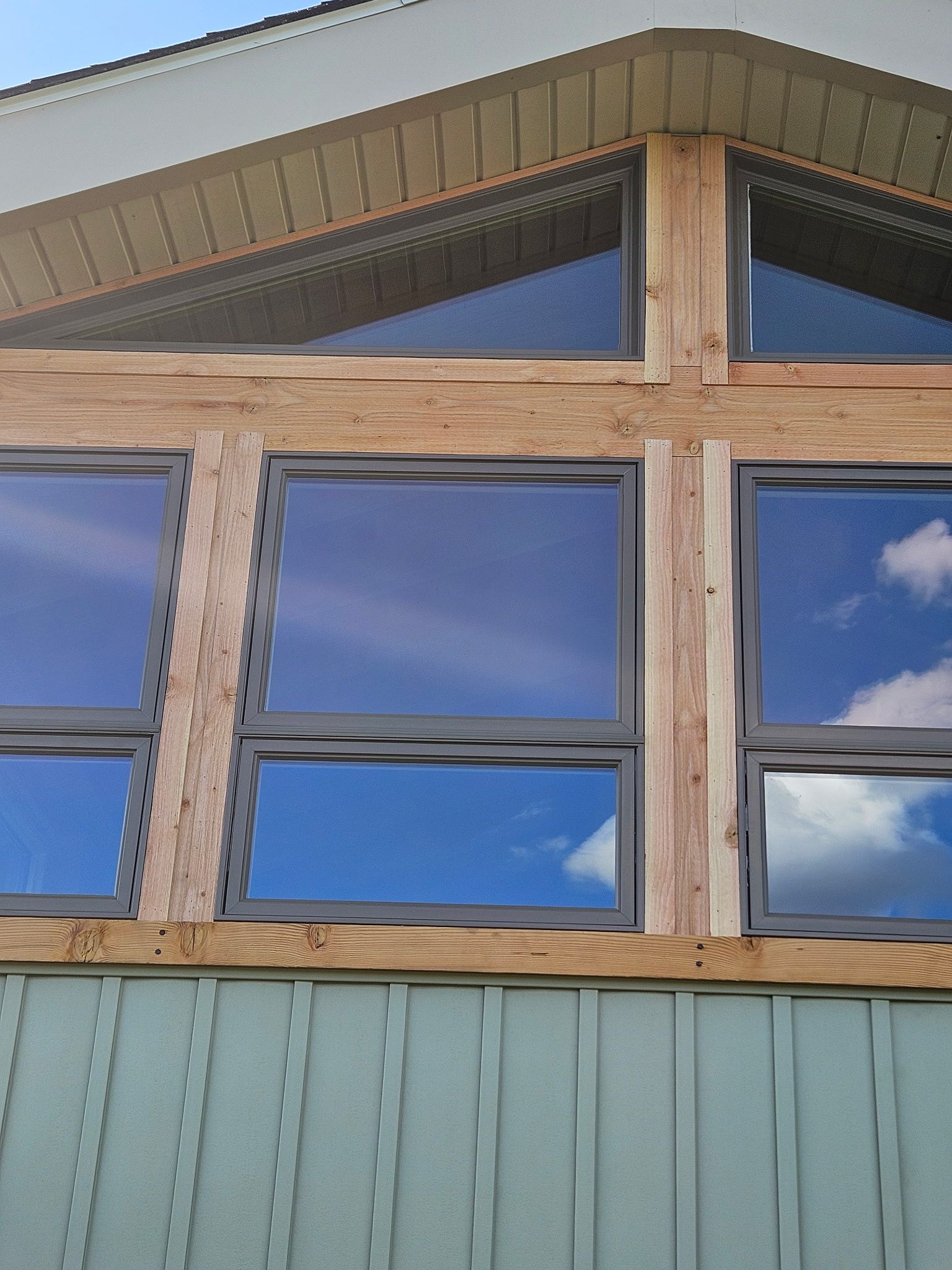 Windows with blue sky reflection, framed by weathered wood on a light-green building.