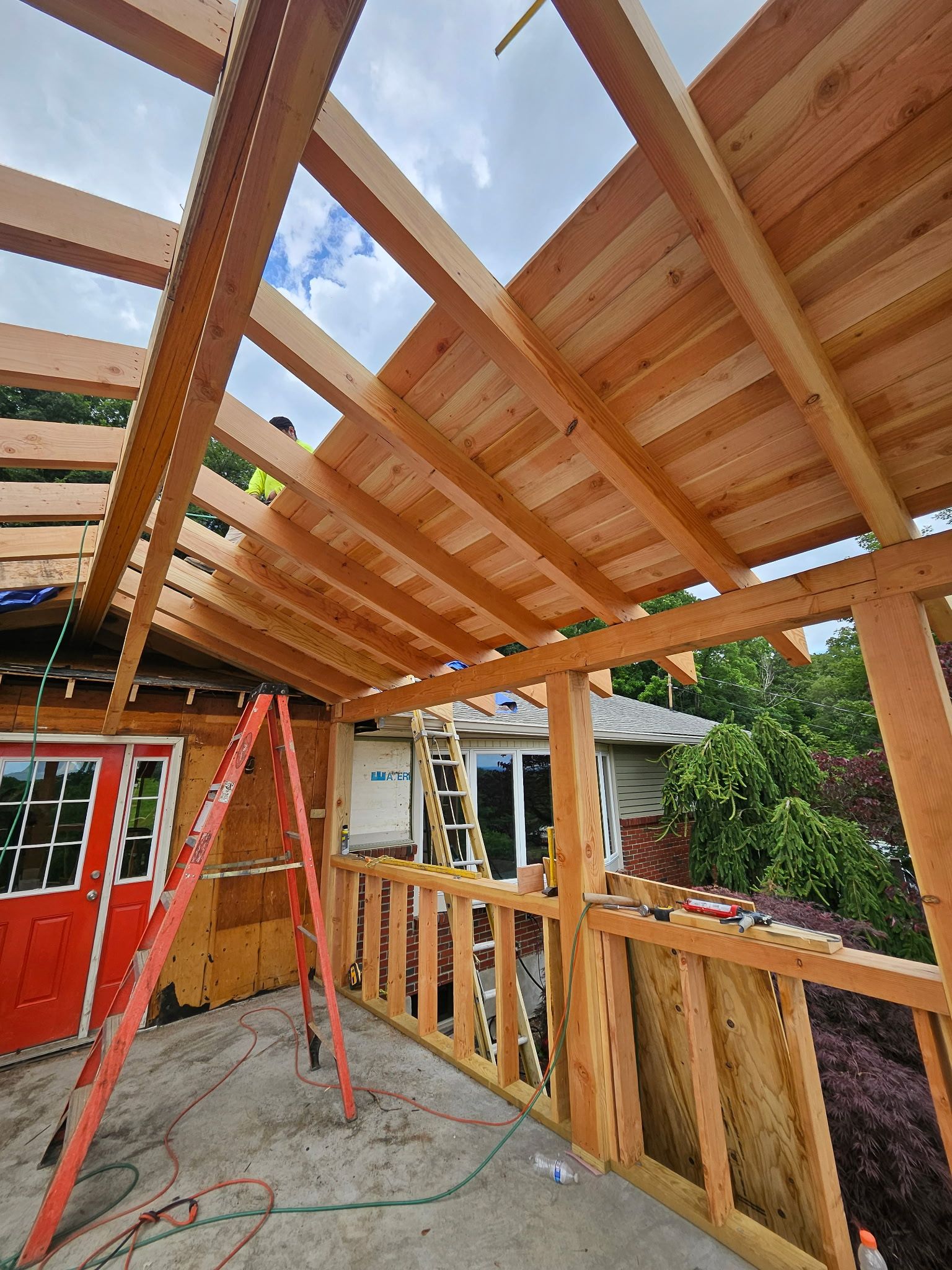 Construction of a wooden patio cover with an orange ladder and a red door in the background.