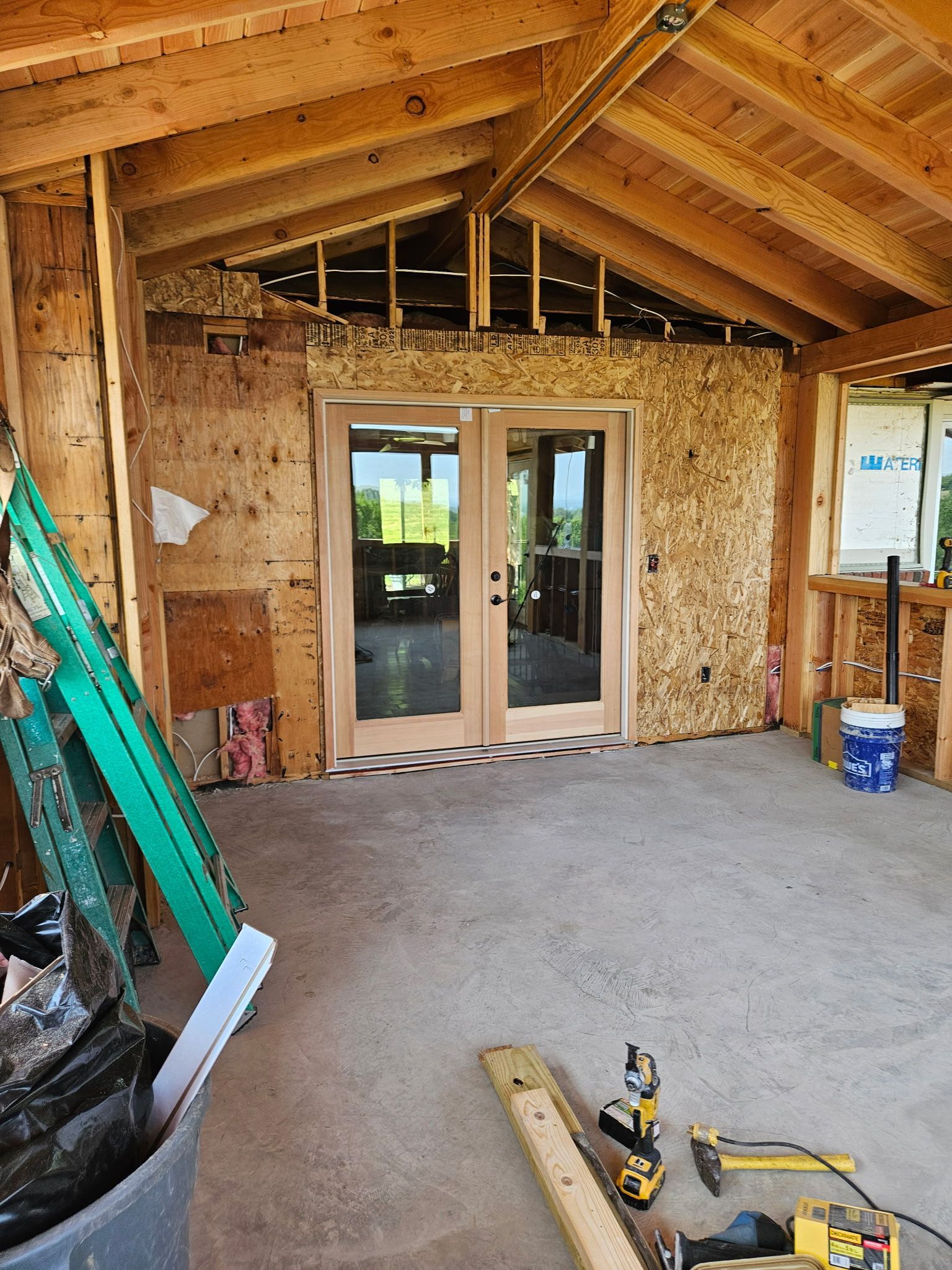 Construction of a covered porch with concrete floor, wood frame, and glass double doors.