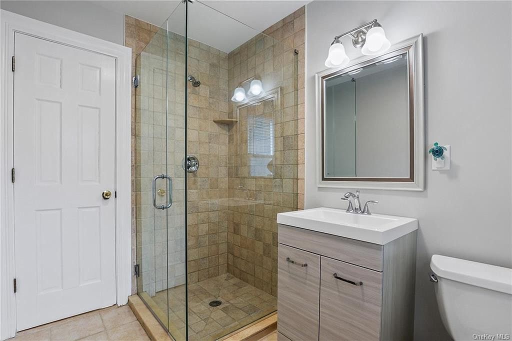 Bathroom with a glass shower, vanity, toilet, and white door.