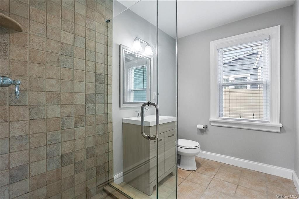 Bathroom with a glass shower, tile walls, vanity, toilet, and window.