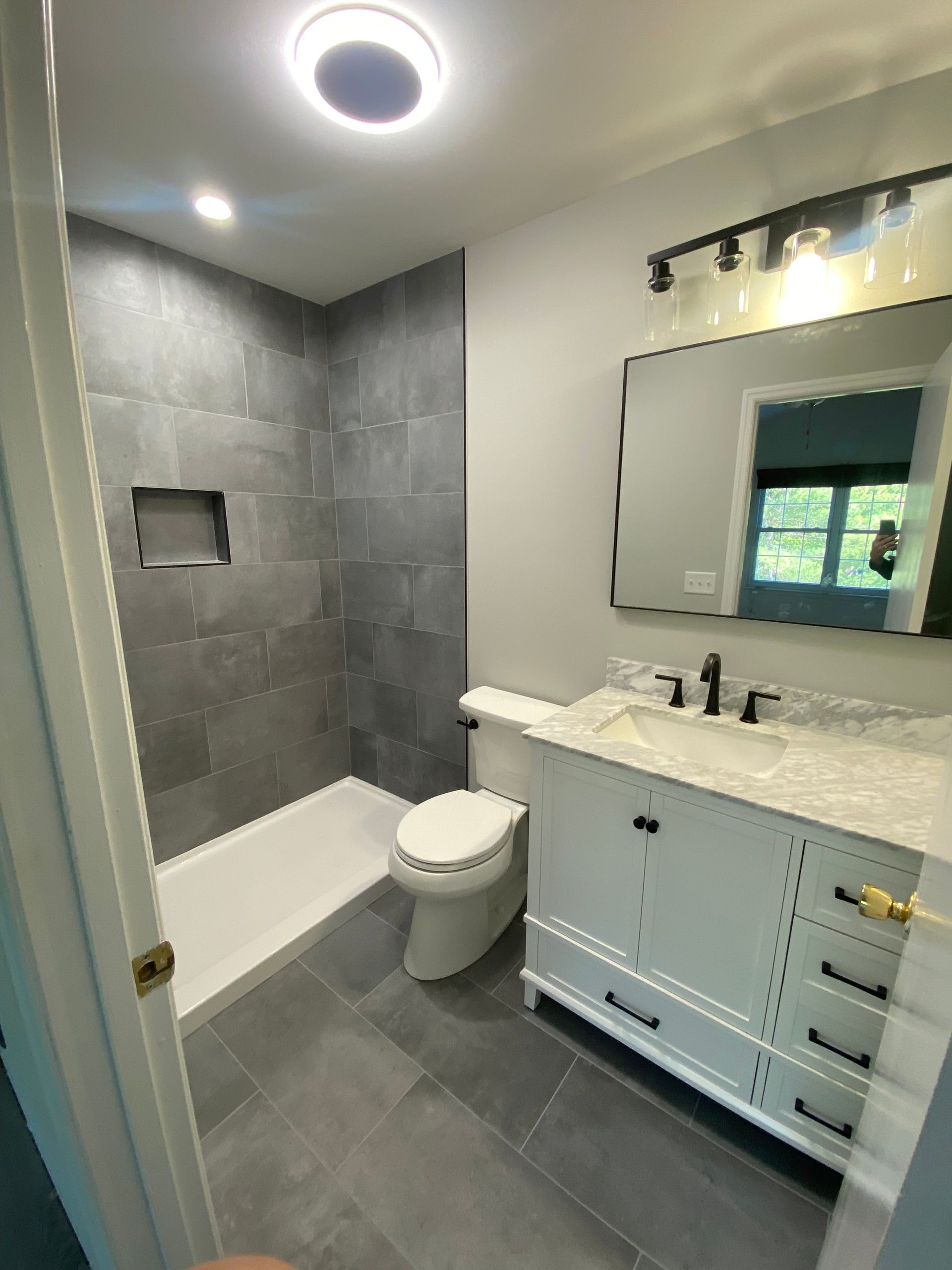 Newly renovated bathroom with gray tile shower, white vanity, and toilet.