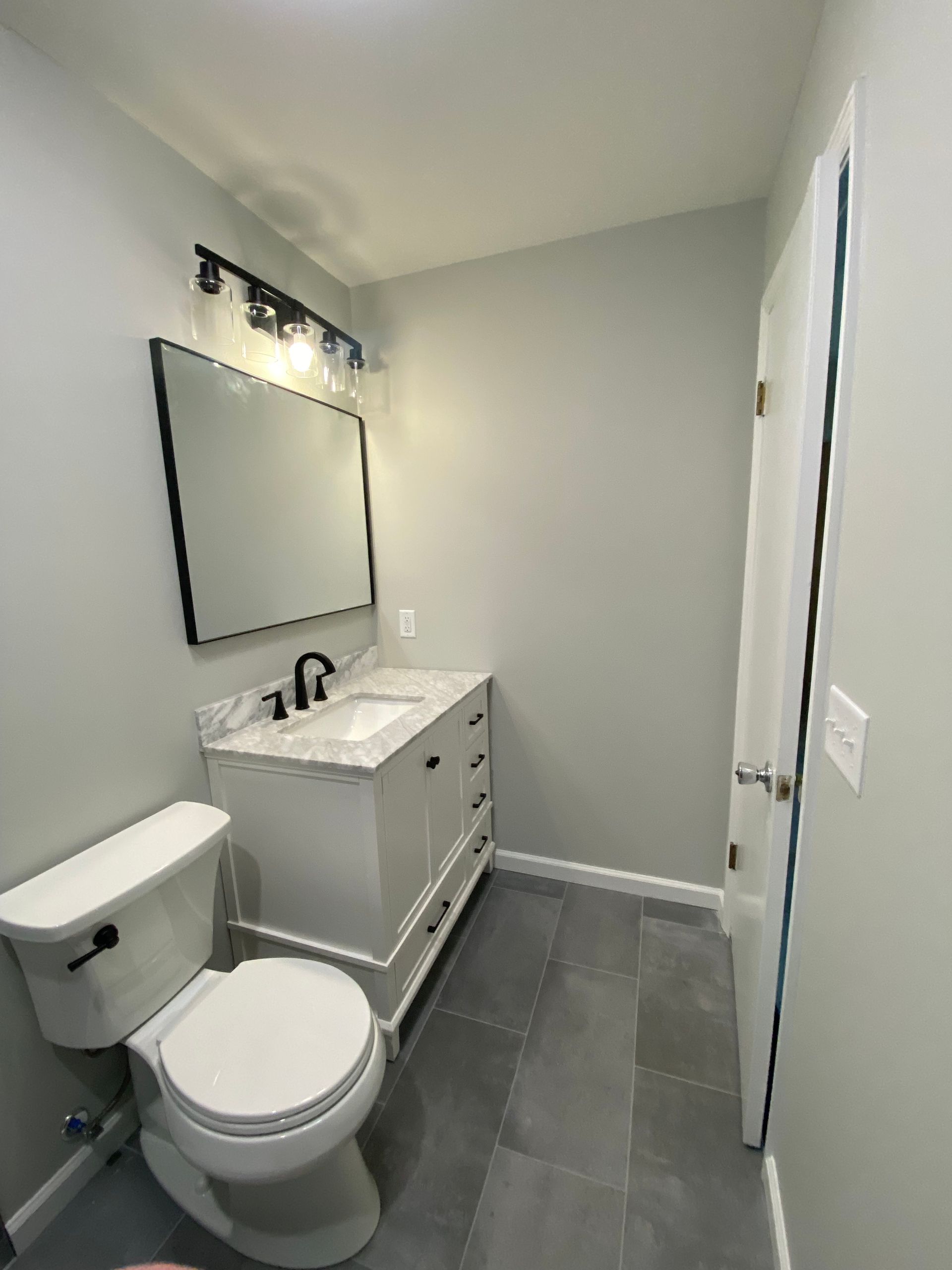 Small bathroom with white vanity, toilet, grey tile floor, and light grey walls.