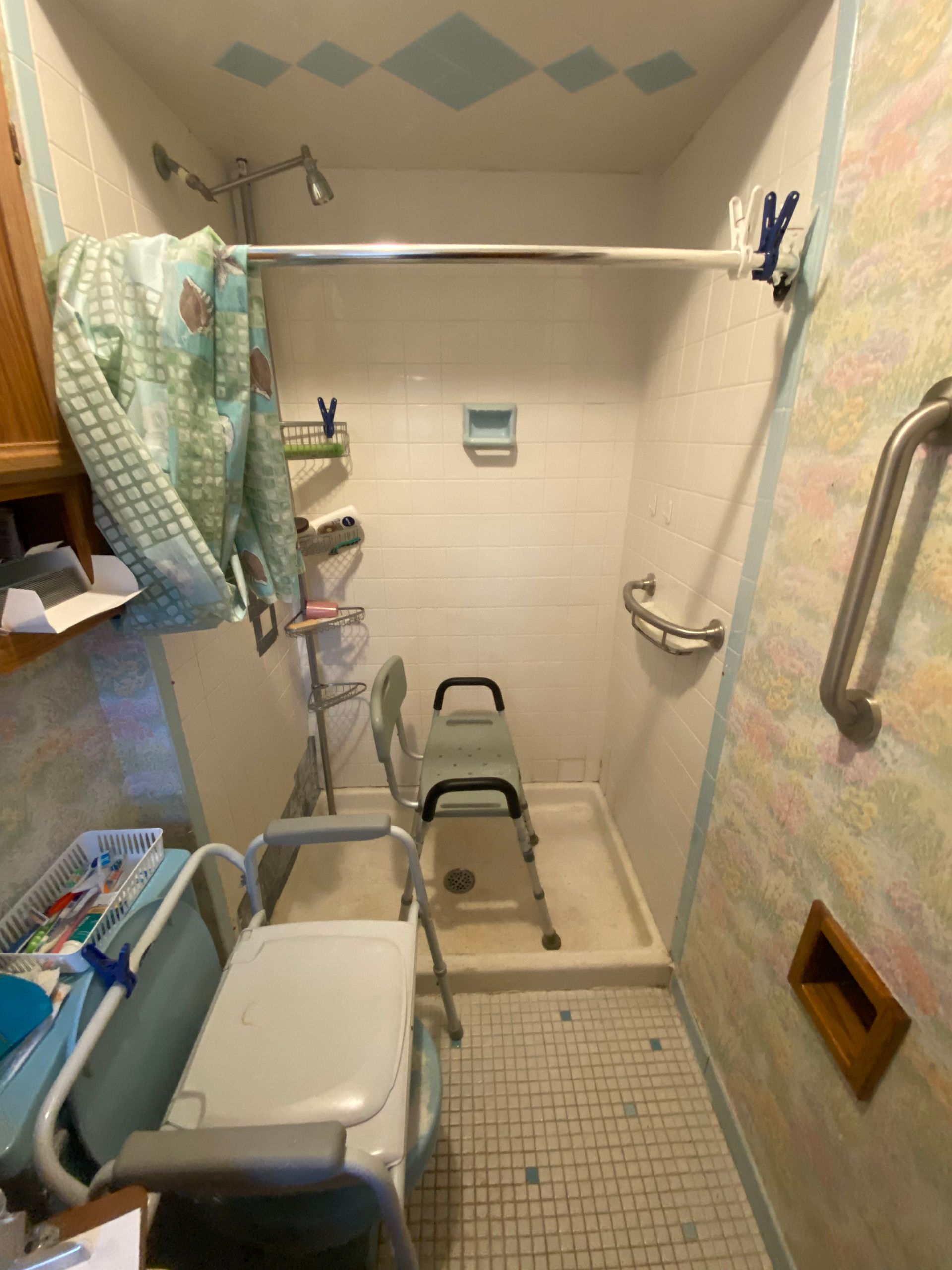 Small shower with safety features, including a grab bar, seat, and wheelchair.