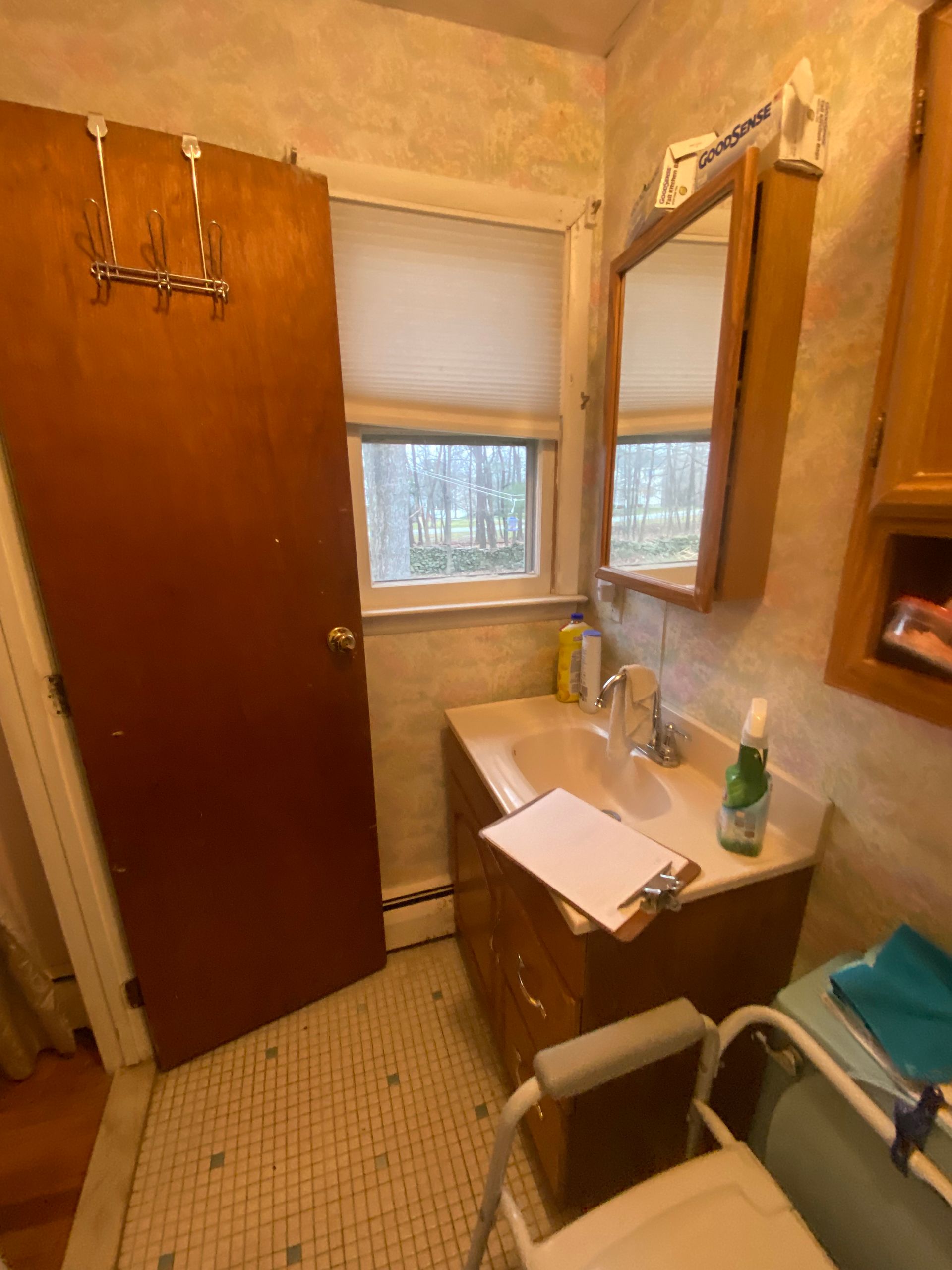 Small bathroom with sink, mirror, window, and open brown door. A walker/shower chair is in front of the sink.