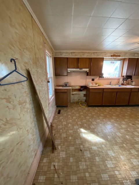 Kitchen with wood cabinets, beige patterned walls, and floor. A window and a coat hanger are visible.