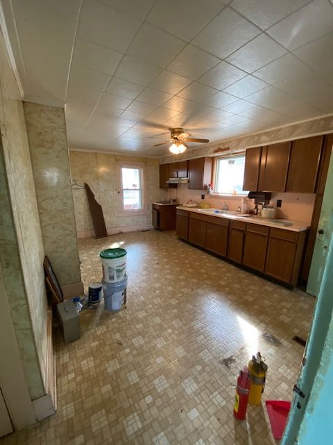 A kitchen with brown cabinets, tiled floor, and a ceiling fan. Construction materials are present.