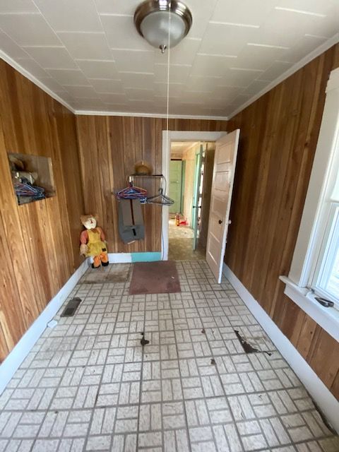Narrow room with wood paneling, tile floor, a doll, open doorway, and a light fixture.
